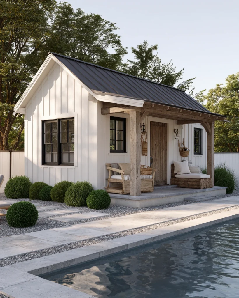White farmhouse-style pool house with board and batten siding beside a backyard pool